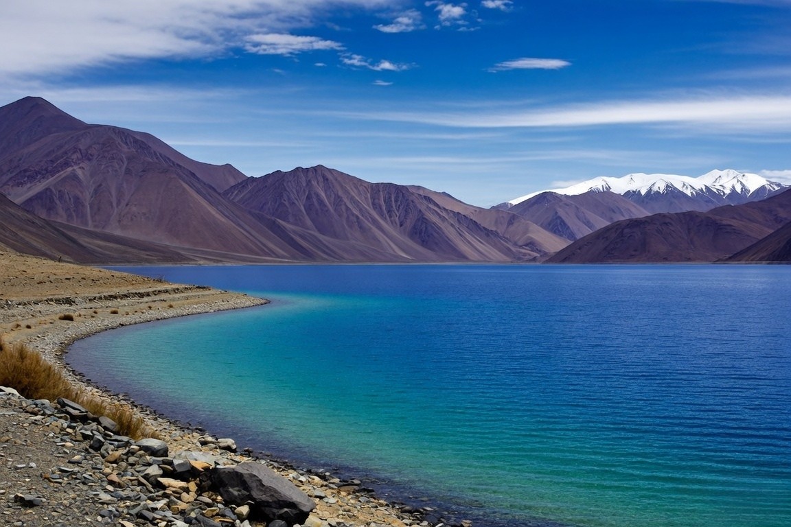 The deep blue and turquoise waters of Pangong Tso lake surrounded by the barren, brown mountains of Ladakh under a clear sky.